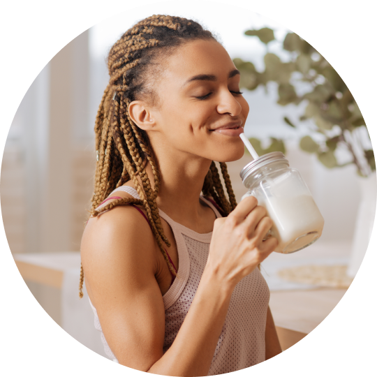 A woman enjoying a plant-based beverage in a cup with a straw.