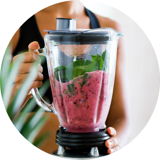 A close-up of a woman making a smoothy of berries and spinach in a blender.