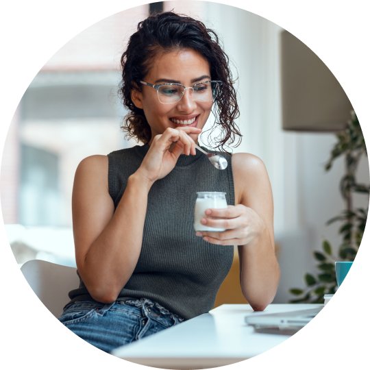 A woman sitting at a table enjoying a yogurt in a small glass container.