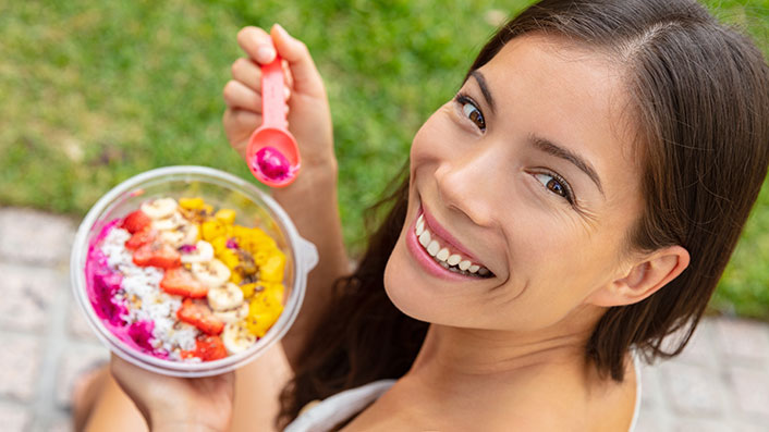 A smiling person eating a bowl of fruit